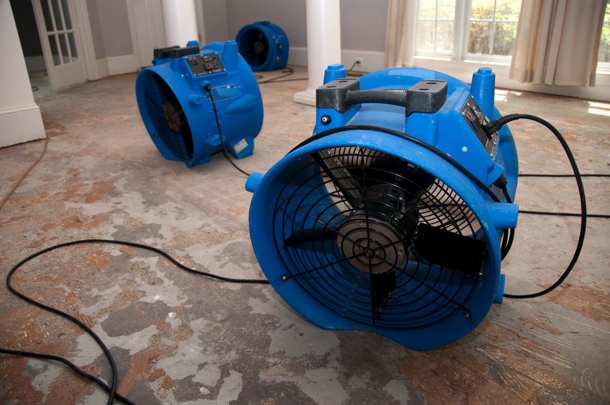 A large room with three huge blue fans being dried after flooding.